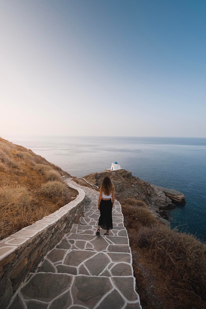 ギリシャのシフノス島の崖の上の教会に向かう途中で歩いている女性