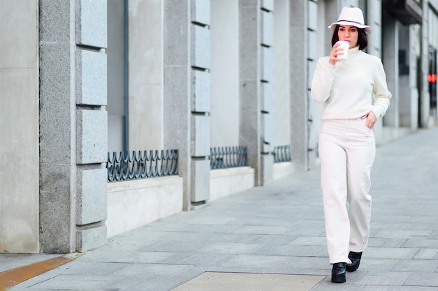 Photo woman walking drinks coffee down the street