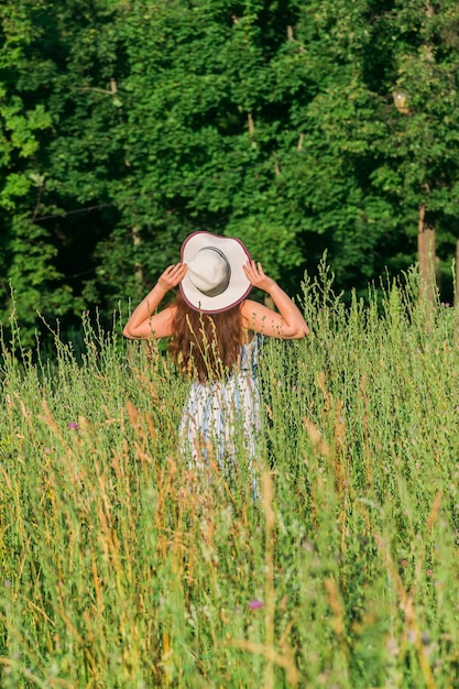 Woman walking in a field in summer sunny day Backside view Summer season and well being concept