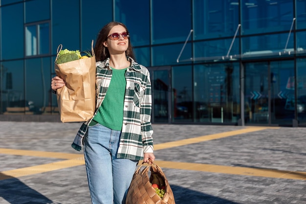 식료품과 함께 쇼핑 종이 가방을 들고 쇼핑 센터에서 걸어가는 여자