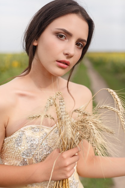 黄金の乾いた草地を歩いている女性。自然な肖像画の美しさ。黄色い麦畑にいる間、彼女の手で小麦の収穫を維持している美しい少女