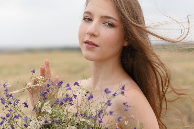 Donna che cammina nel campo di erba secca dorata. bellezza naturale del ritratto. bella ragazza in un campo di grano. giovane donna in un vestito beige che tiene un mazzo di fiori di campo.