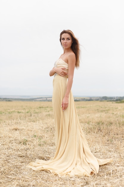 Woman walking in golden dried grass field. Natural portrait beauty. Beautiful girl in a wheat field