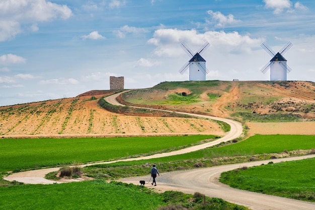 Woman walking her dog in the countryside with a hill with large windmills in the background.