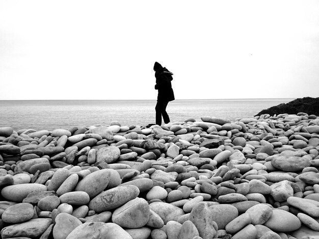 Foto donna che cammina su ciottoli sulla spiaggia contro un cielo limpido