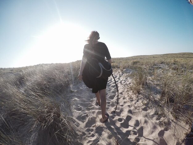 空に逆らってビーチで砂の上を歩く女性