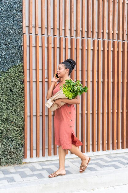 Photo woman walking and talking on the phone with fresh produce