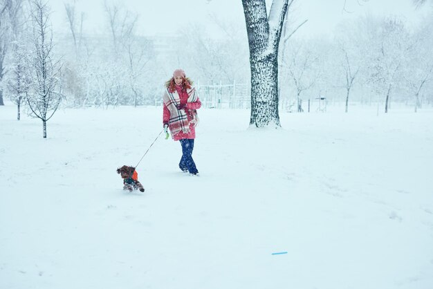 눈 덮인 공원에서 그녀의 강아지와 함께 산책하는 여자
