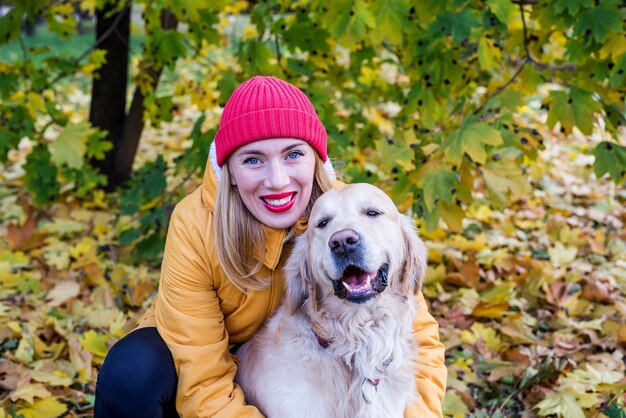 Donna che cammina con il suo cane da riporto tra le foglie gialle autunnali