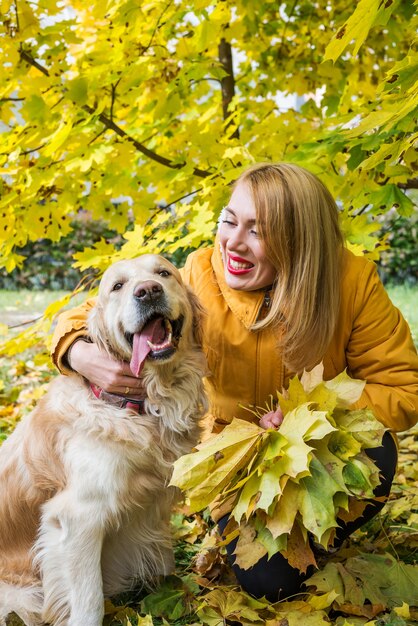 Woman walking with her retriever among autumn yellow leaves