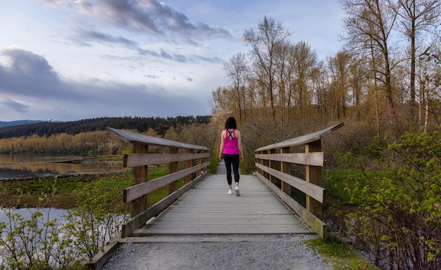 Photo woman walking on a wooden path with green trees in shoreline trail