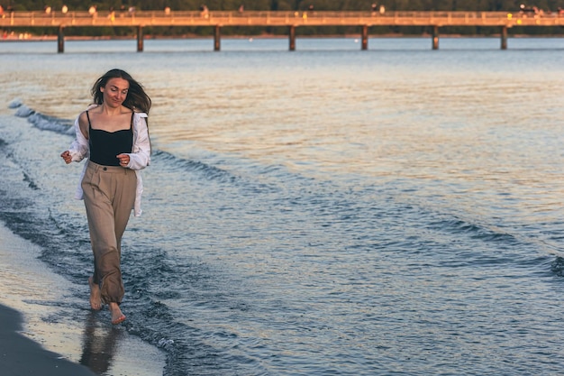 Una donna cammina lungo il mare a piedi nudi allo spazio della copia del tramonto