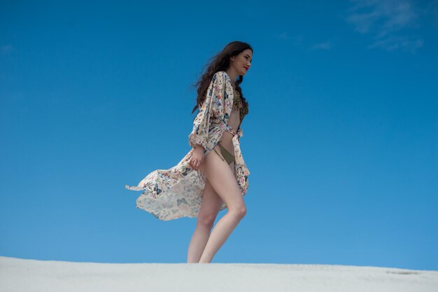 A woman walks on a beach wearing a floral kimono.