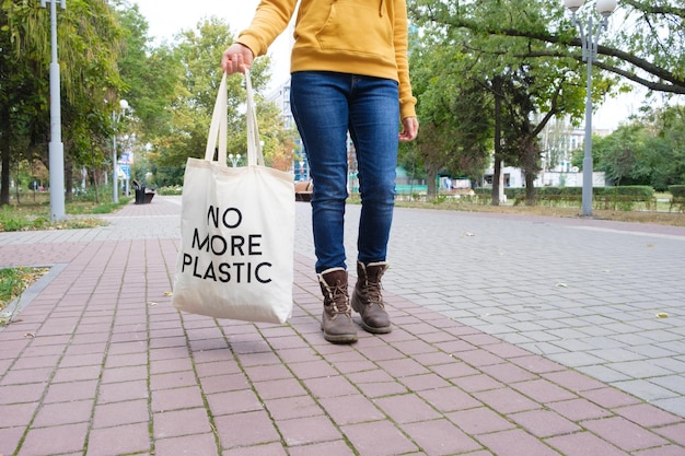 A woman walks down the street and holds a reusable cloth bag that says No more plastic