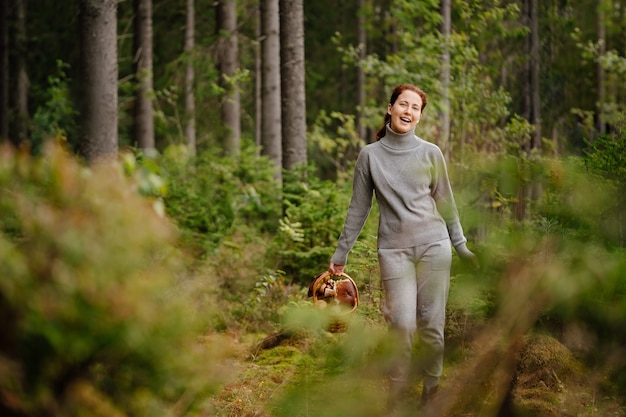 Фото Женщина гуляет в летнем лесу, собирая грибы в корзину. концепция похода и экологически чистые продукты.