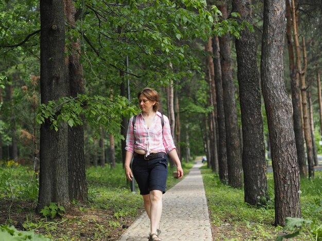 Photo a woman walks in the summer in the park in sunny weather she walks along a forest path