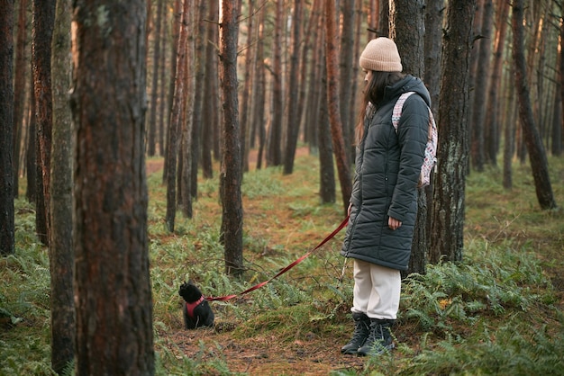 Woman walks with cat on a leash in the forest Black cat on a leash walking along the road in the woods