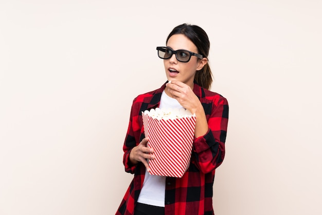 Woman over wall with 3d glasses and holding a big bucket of popcorns while looking side