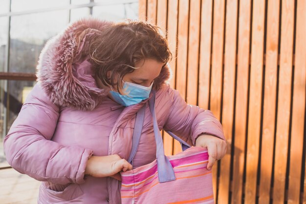 Woman in warm coat after shopping holding cotton bag with\
purchases sunny winter morning in front of supermarket