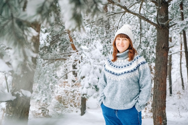 雪に覆われた森の背景に暖かい帽子とセーターを着た女性