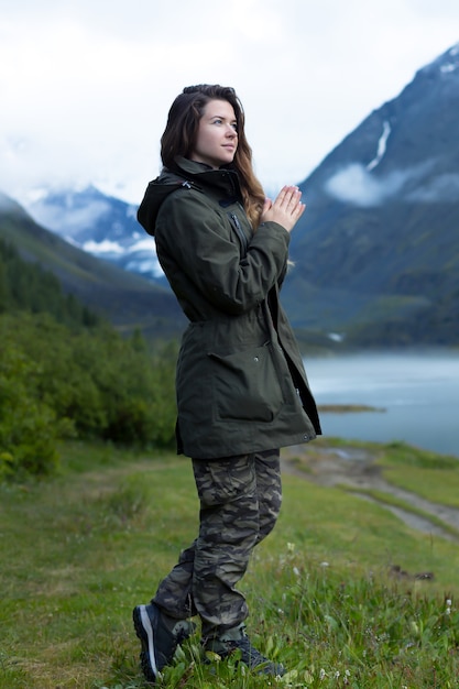 A woman in a warm jacket with long hair stands against a background of mountains in the fog in cold damp weather