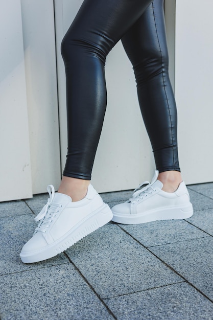 A woman in a warm sweater and black leather leggings in white autumn sneakers Women's shoes made of genuine leather