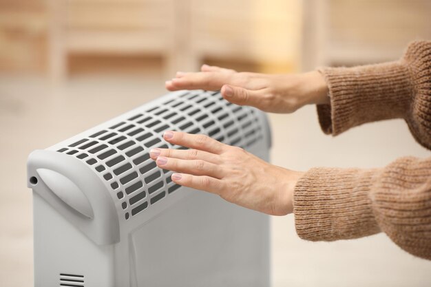 Photo woman warming hands on electric heater at home closeup