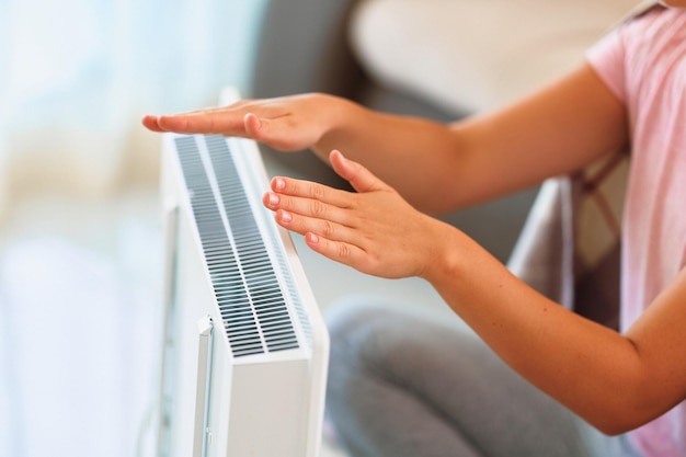 Woman warming hands near electric portable heater at home