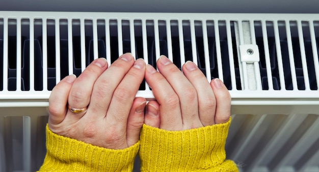 Photo the woman warms her hands on the radiator