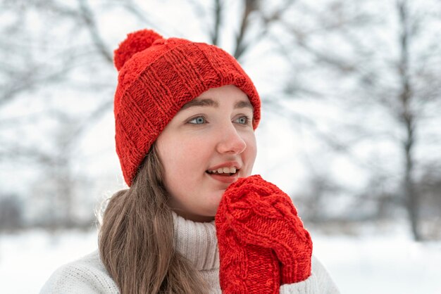 Woman warms up hands in woolen clothes outdoors cold weather Young woman in knitted red hat and mittens winter park