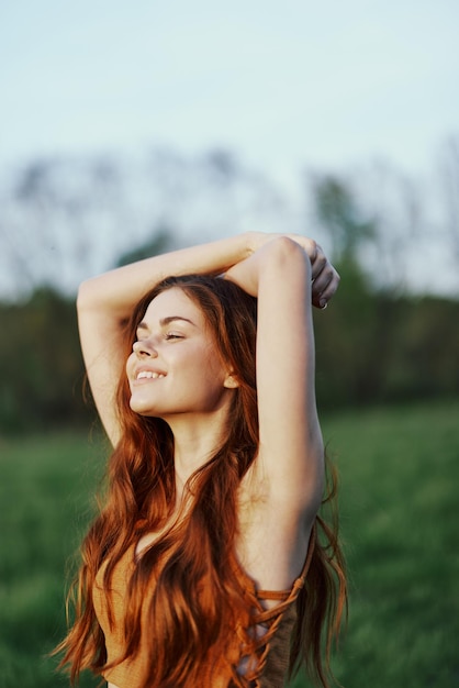 A woman warms up and stretches her arms up in nature in a green park after an outdoor sports workout in the sunset sunlight The concept of a healthy lifestyle and an athletic body