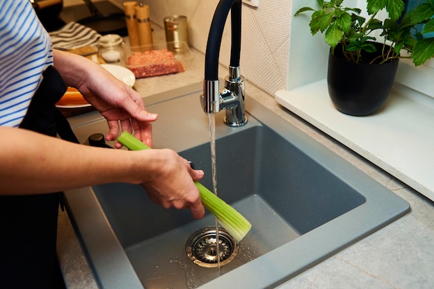 Woman wash fresh celery in kitchen