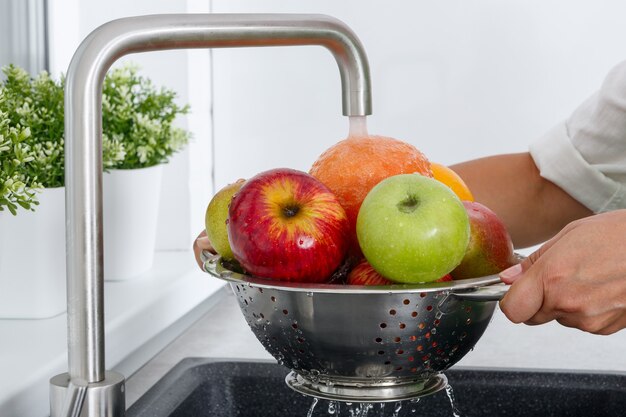 A woman washes fruits by running tap water in the kitchen