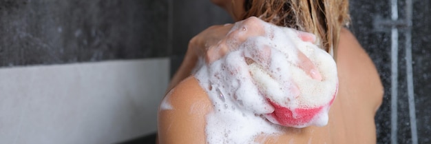 Woman washes her body with a sponge and shower gel