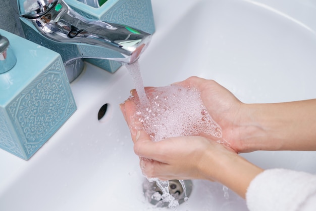 Woman washes her hand in the bathroom sink