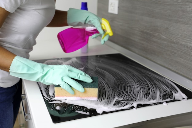 Woman washes the hob with a sponge and detergent with foam. Close up.