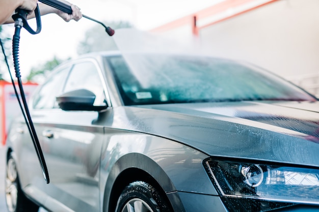 高圧水機を使用して洗車場で車を洗う女性。