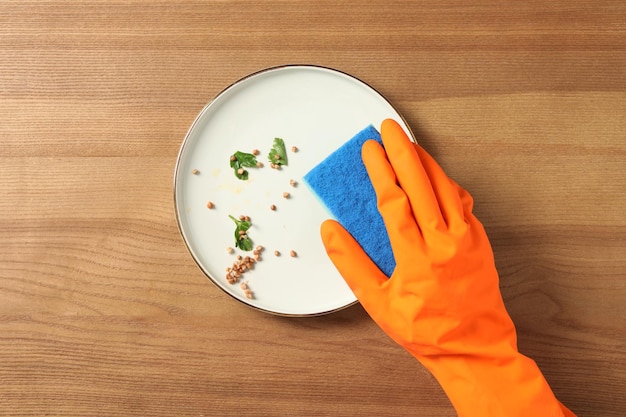 Photo woman washing dirty plate at wooden table top view