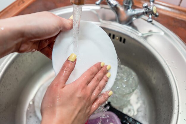 Woman washing dishes in kitchen sink closeup view Cleaning chores