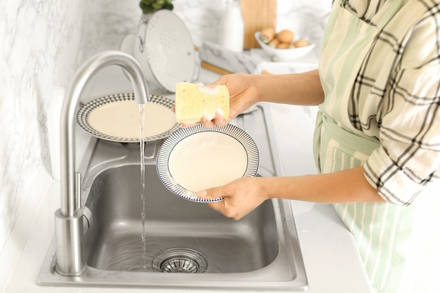 Woman washing dishes in kitchen sink