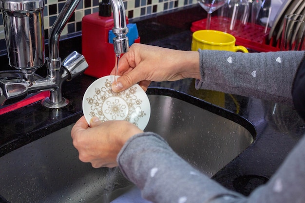 Woman washing dishes plate under running water