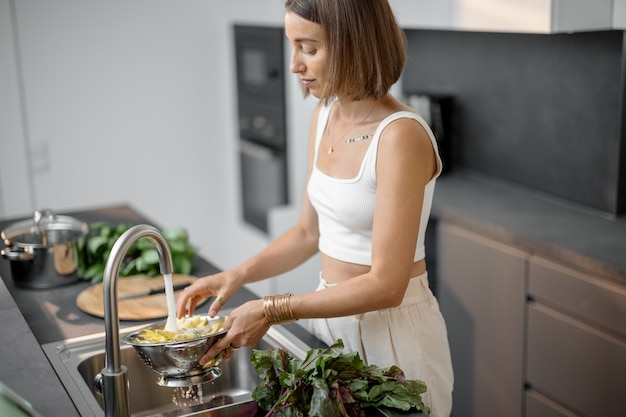 Женщина моет свежие овощи и зелень в раковине