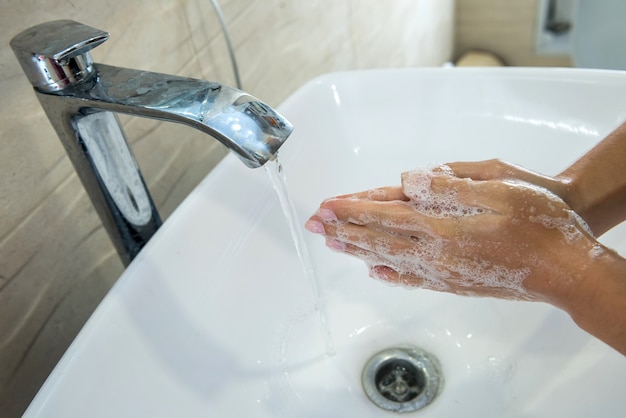 Woman washing hands with disinfectant soap and water in bathroom