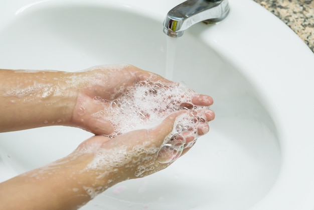 Woman washing hands with soap under the faucet with water in the bathroom.