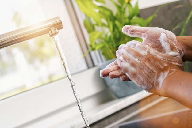 Woman washing of hands with soap under running water in the kitchen