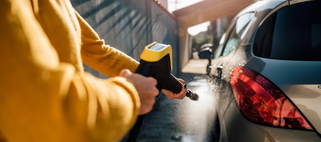 Donna che lava la sua auto con idropulitrice