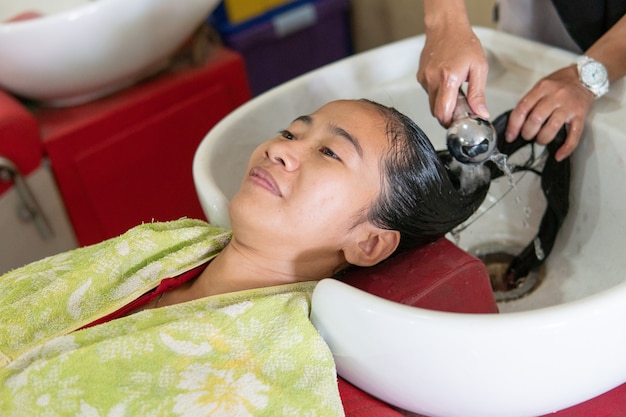 The woman washing her hair by a hairstylist in salon