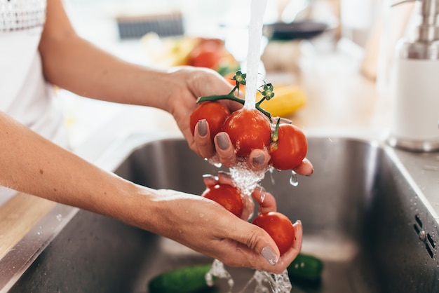 Woman washing tomatoes in kitchen sink close up.