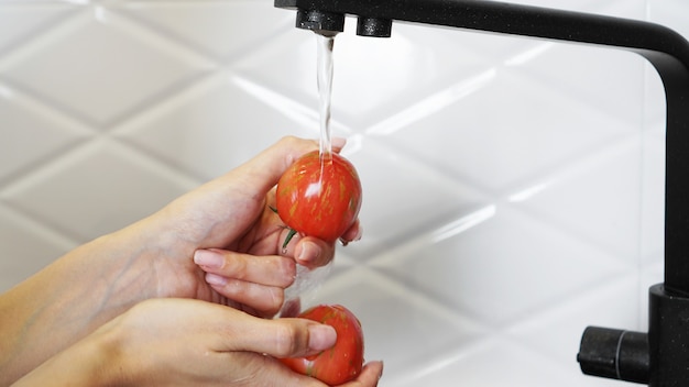 Donna che lava i pomodori e il pomodoro nelle sue mani - sfondo bianco della cucina