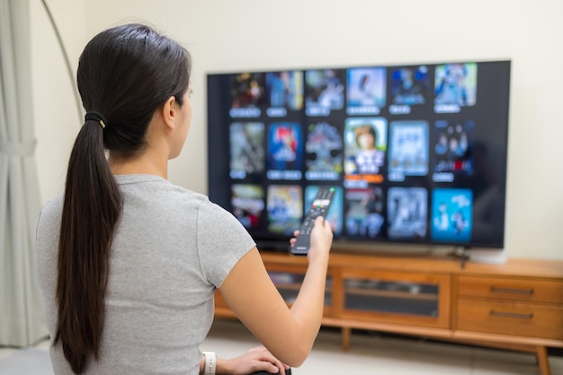 여성은 TV를 보고 집에서 프로그램을 선택하기 위해 리모컨을 사용합니다.